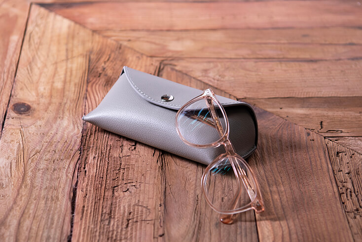 A gray glasses case with glasses on a wooden table