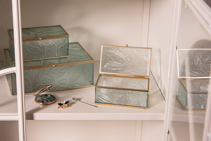 Three glass jewelry boxes with a makeup mirror and brooches