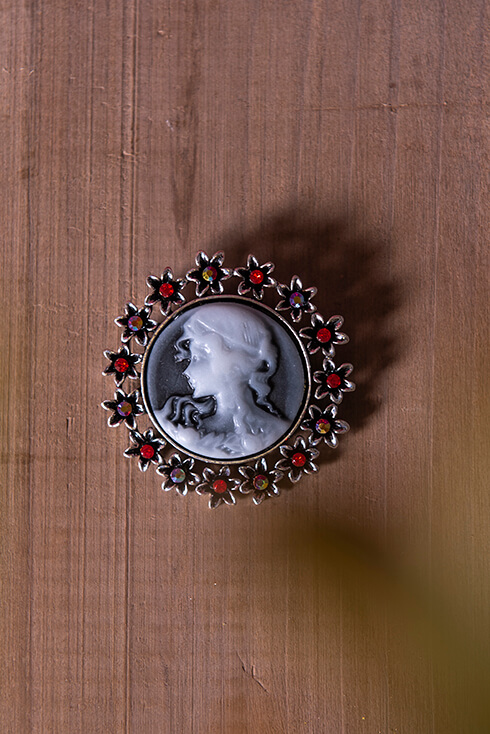 A pin of a woman with red flowers around it with small diamonds inside
