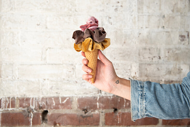 An ice cream cone with three scrunchies on it in yellow, purple and pink