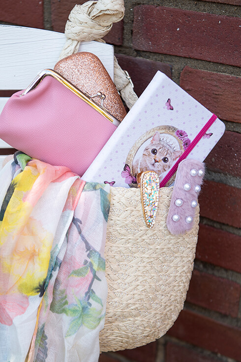A brown basket with a notebook, pink wallet, two hairpins and a summer scarf
