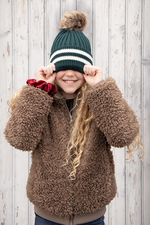 A girl wearing a green winter hat with a red scrunchie around the wrist