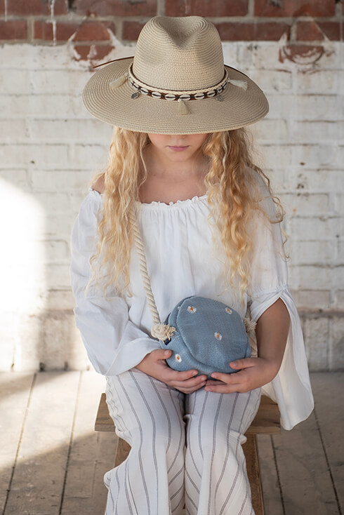 A girl with a white blouse, a blue handbag with daisies, and a light beige summer hat