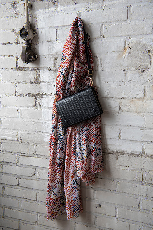 An autumn scarf and black handbag hanging on a white brick wall