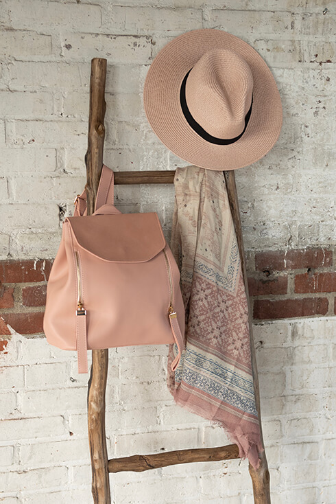 Eine Holzleiter, an der ein rosa Rucksack, eine rosa Mütze und ein bunter Sommerschal hängen