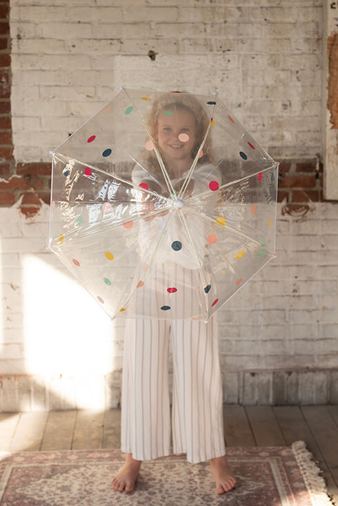 Una ragazza con in mano l'ombrello di un bambino con punti colorati