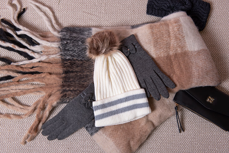 Een verzameling winteraccessoires, waaronder een witte wintermuts, grijze handschoenen en een dikke bruine wintersjaal