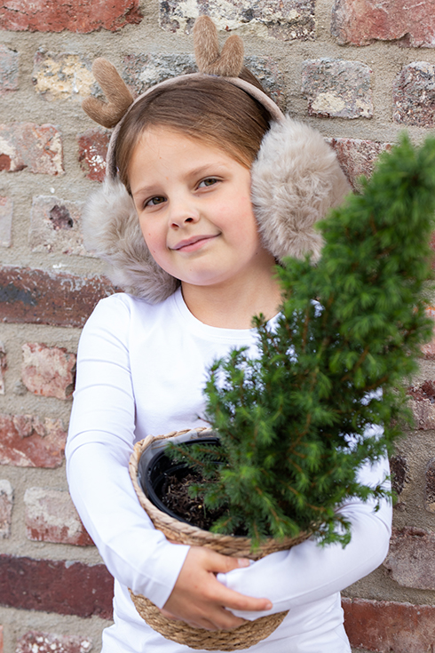 Una ragazza che indossa un piccolo albero di Natale e un paraorecchie beige da bambino