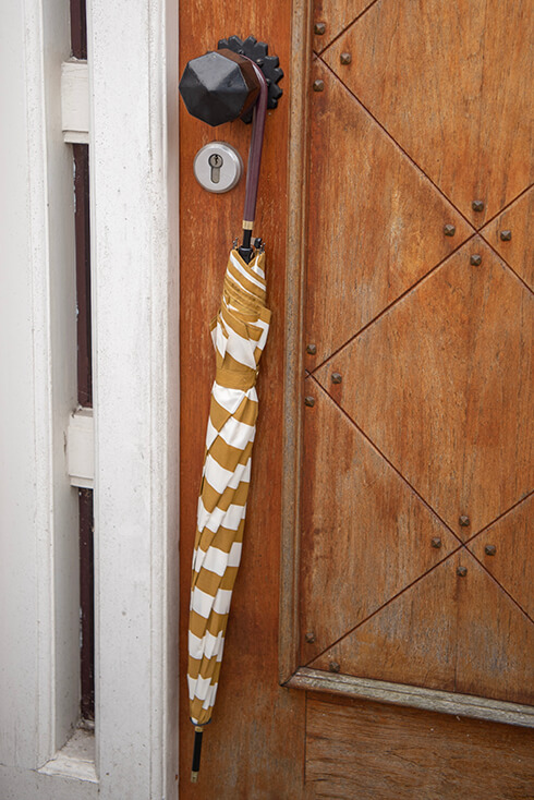 A closed umbrella with white and yellow stripes hanging on a door