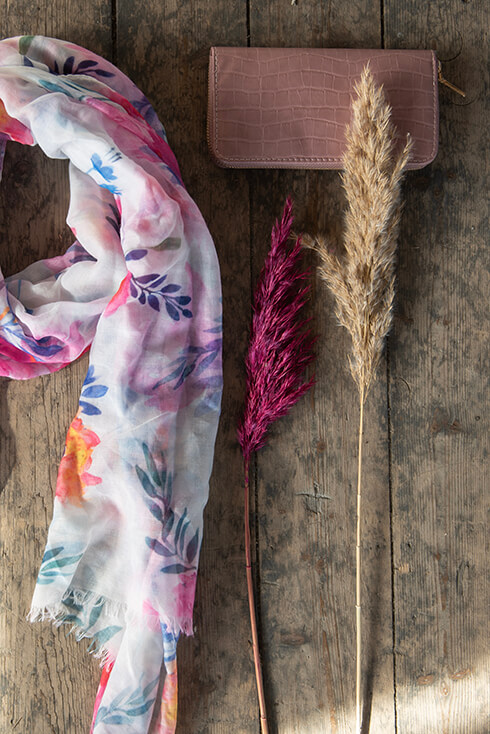 A floral summer scarf with a pink wallet and two dried flower branches