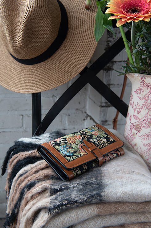 A floral brown wallet with embroidery on a black wooden chair and a thick winter scarf