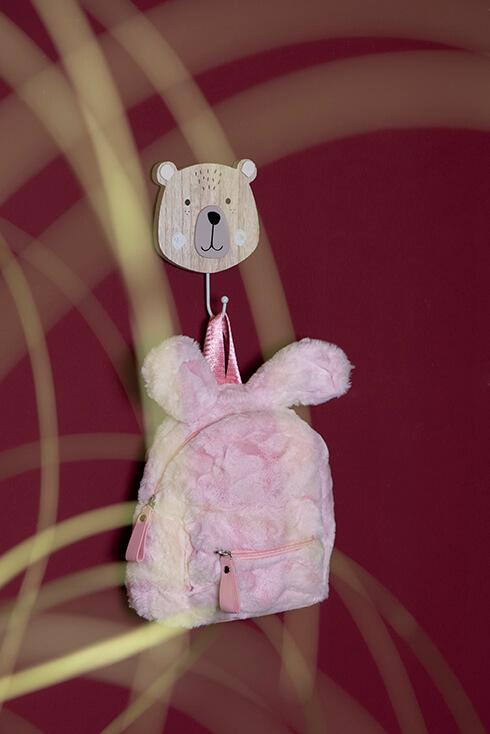 Een roze kinderrugzak die aan een beren wandhaak hangt