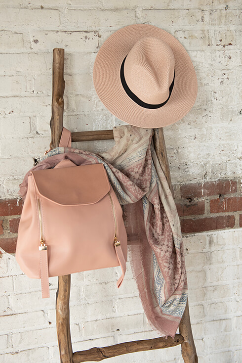 A wooden ladder with a pink backpack, pink summer hat, and a summer scarf hanging on it