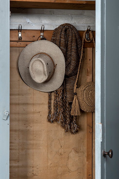 A cupboard where a beige hat, brown winter scarf, and a brown handbag are stored