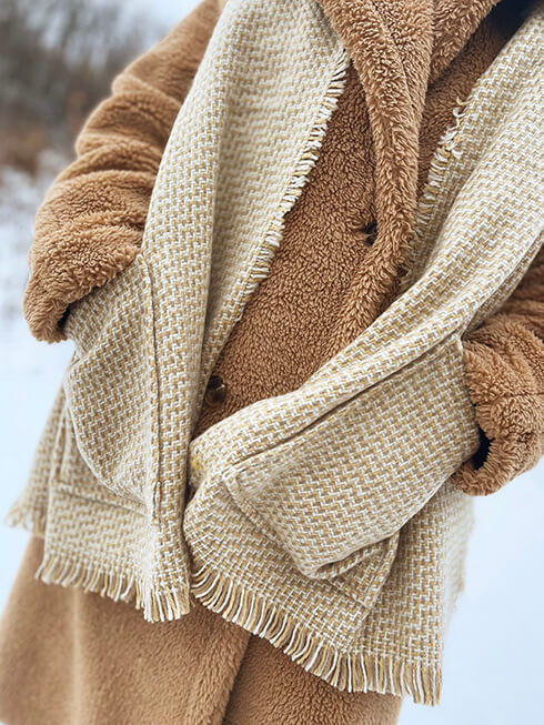 Someone in a beige winter coat with a beige winter scarf with hand pockets