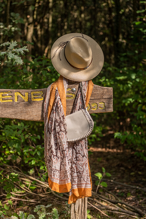 Een houten bord met daaraan een beige hoed, fleurige zomersjaal en een grijze handtas