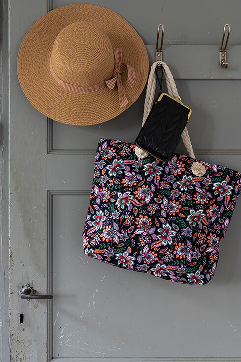 Ein brauner Hut und eine Strandtasche mit Blumenmuster mit einer schwarzen Geldbörse, die an einer grauen Tür hängen