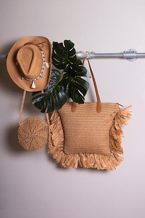Ein Eisenstab, an dem ein Cowboyhut, Palmblätter, eine Korbhandtasche und eine Strandtasche hängen