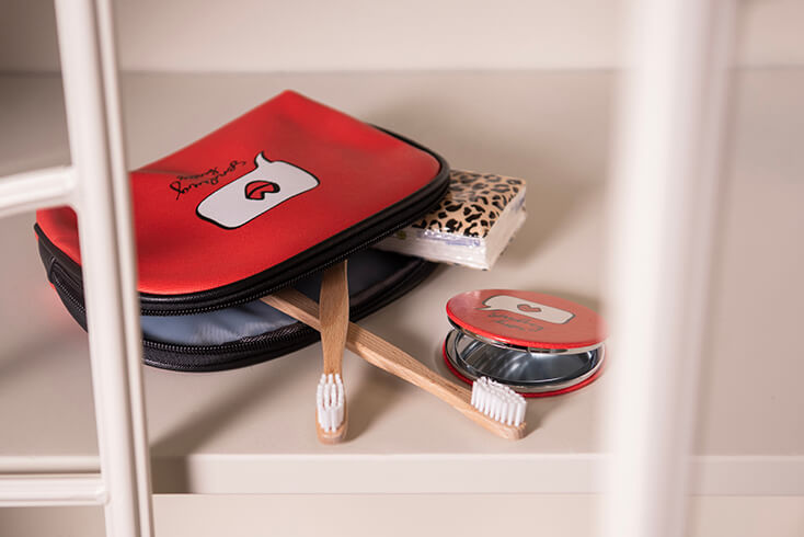 A red toiletry bag with two wooden toothbrushes and tissues inside, and next to it, a red makeup mirror