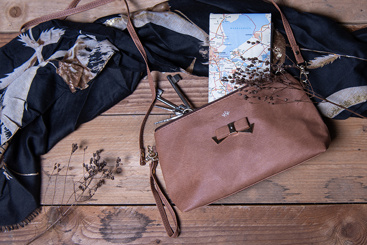 A brown toiletry bag with a bow and inside it, a map and another black autumn scarf
