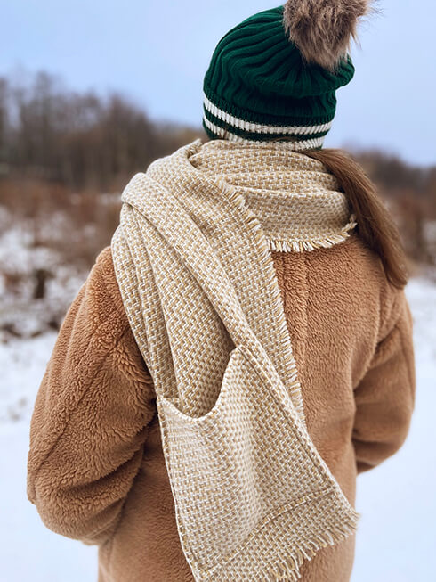 Someone with a green winter cap and a beige winter scarf with pockets