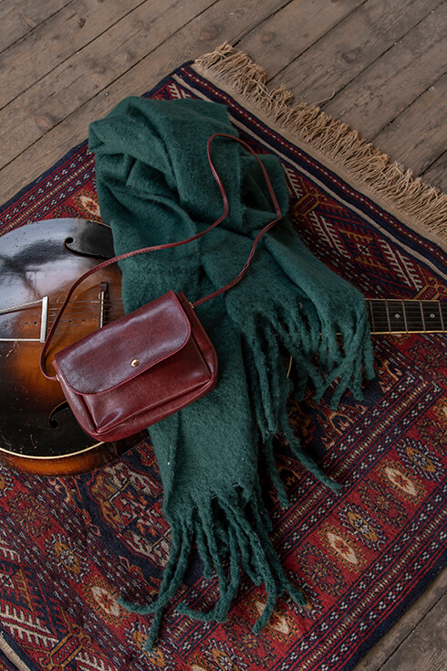 Een dikke groene wintersjaal en een bruine handtas op een gitaar