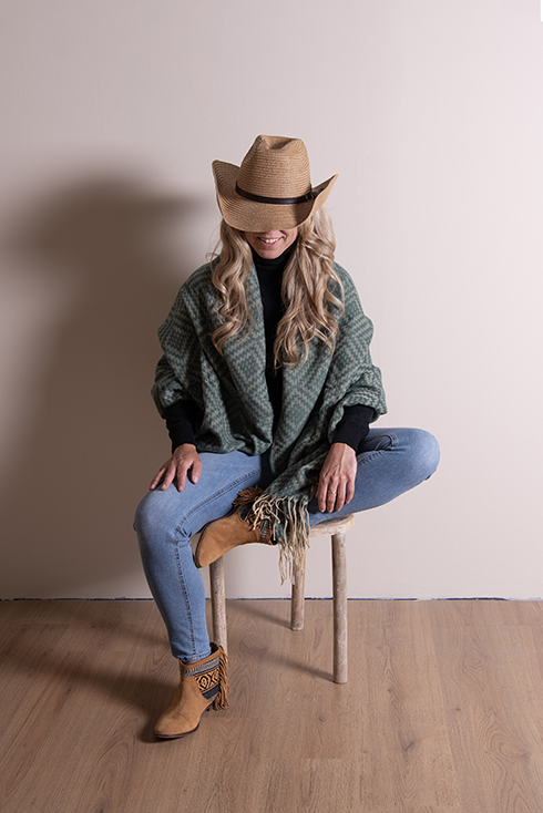 Someone sitting on a wooden stool with a cowboy hat and a thick green winter scarf