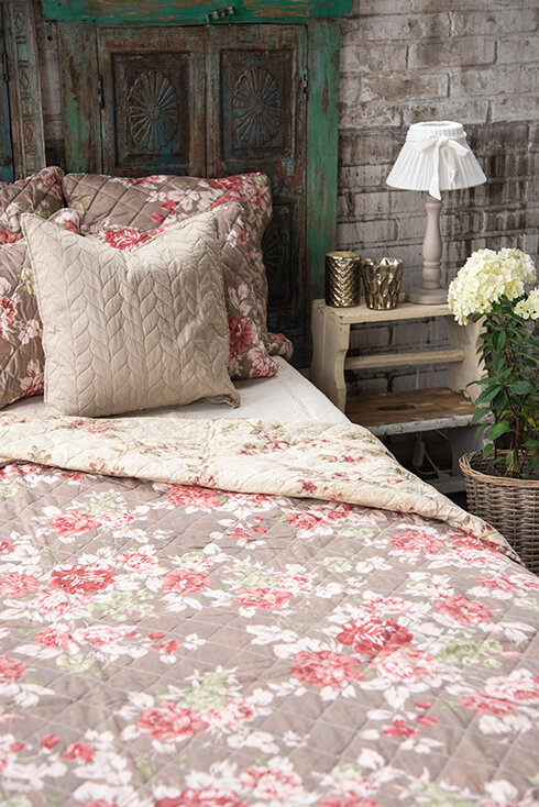 Ein gemachtes ländliches Bett mit einer braunen Bettdecke mit rosa Pfingstrosen und Kissen