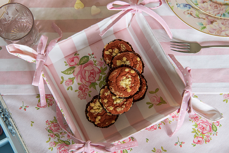 Ein romantischer Brotkorb mit rosa und weißen Streifen und schönen Rosen, gefüllt mit roten Samt-Cupcakes