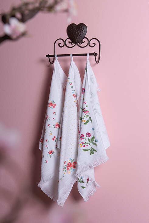 Un porte-serviettes en métal où trois gants de toilette à motif floral sont accrochés