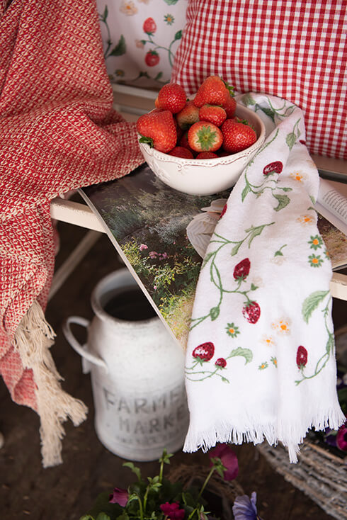 Een wit landelijk kommetje gevuld met aardbeien met ernaast een aardbeien gastendoekje