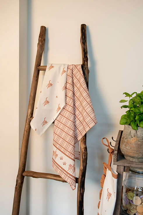 A wooden towel holder with two tea towels featuring kittens on them