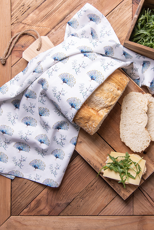 A loaf of bread on a cutting board with a peacock-themed tea towel over it