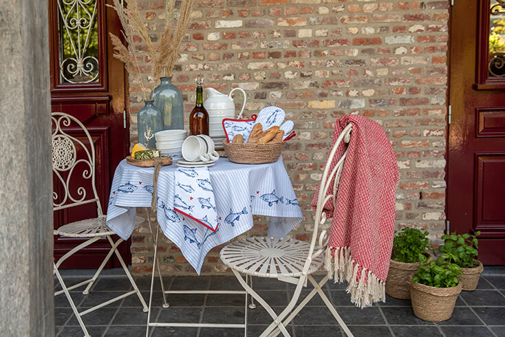 A bistro set in the garden with tableware, kitchen accessories, and kitchen textiles, and a red throw hangs on the garden chair