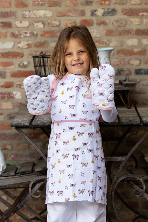 A girl wearing a children's apron with butterflies and two children's oven mitts