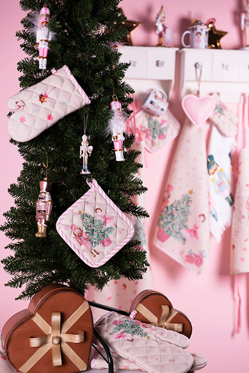 Ein künstlicher Weihnachtsbaum mit pinken Nussknackern, Weihnachts-Kinderbackhandschuhen und einem Weihnachts-Kind Topflappen