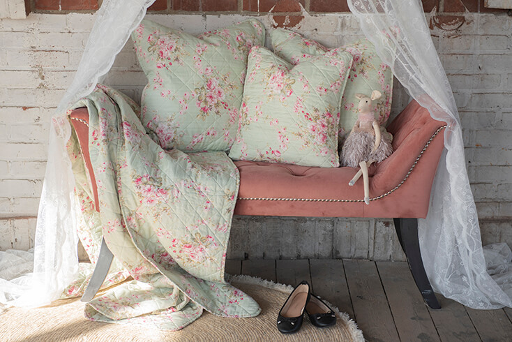 Un banc rose avec trois coussins de chambre, un couvre-lit et une moustiquaire sur un baldaquin de lit, et un tapis rond est posé au sol