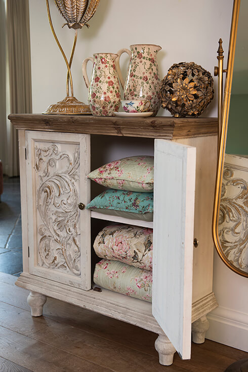 A shabby chic storage cabinet where vintage cushions and bedspreads are stored