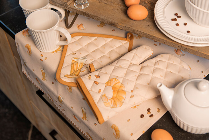 Ein Kücheninsel mit einem Topflappen mit Kaffee- und Croissantsmotiv und einem Ofenhandschuh mit Croissants und Kaffeebohnen