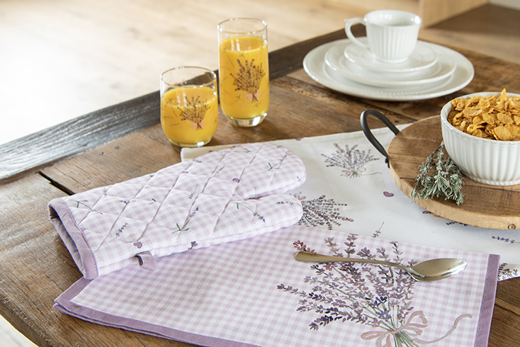 Een tafel met een lavendel servet, lavendel ovenwant en twee drinkglazen met een bosje lavendels erop