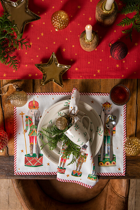 Een gedekte Kersttafel met een stoffen placemat met notenkrakers en Kerstservies met hulstbladeren