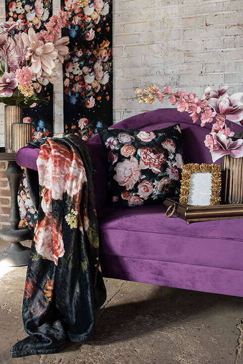 Un divano viola in stile barocco con un cuscino decorativo e una coperta appesa sul bracciolo