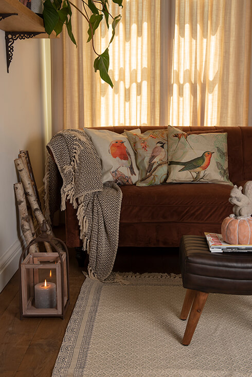 Un divano in stile country con tre cuscini decorativi a tema uccelli e una grande coperta grigia