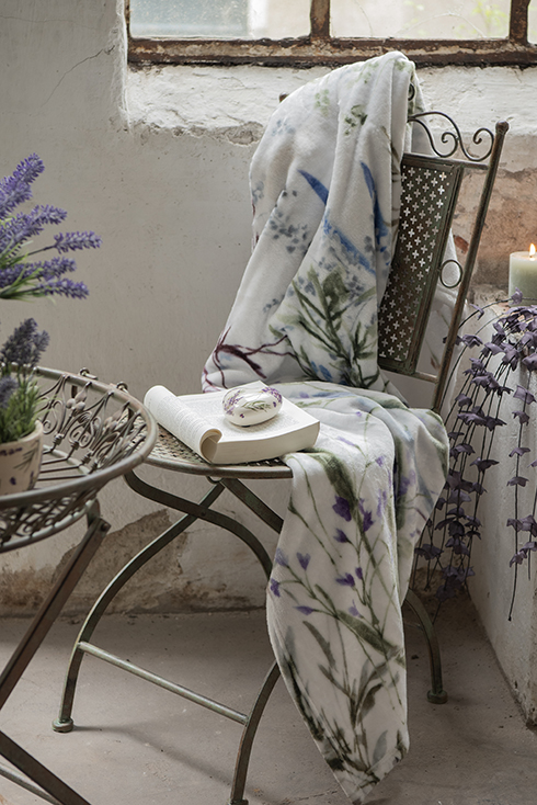 Une chaise de jardin en fer avec un plaid en lavande et un cœur en céramique avec des brins de lavande