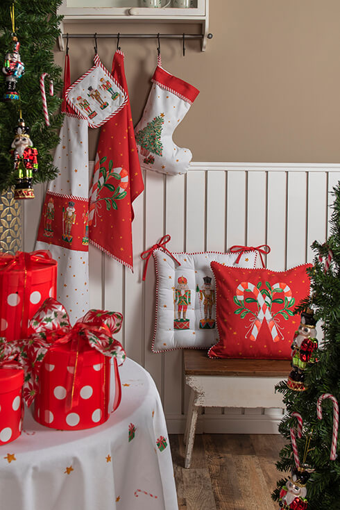 Een houten bankje met twee Kerstkussens erop en een kapstok waar een Kerstschort, Kerstsok, Kersttheedoek en Kerstpannenlap aanhangt