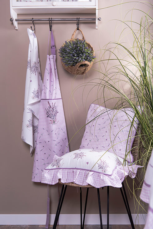 Eine Garderobe mit einem Lavendel-Geschirrtuch und Lavendel-Shorts, und ein Rattanstuhl mit einem Dekokissen und einem Stuhlkissen mit Lavendel darauf