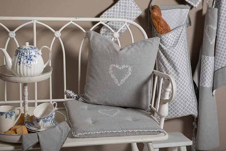 Una panca da giardino bianca con un cuscino per sedia country e un cuscino decorativo con un cuore ricamato