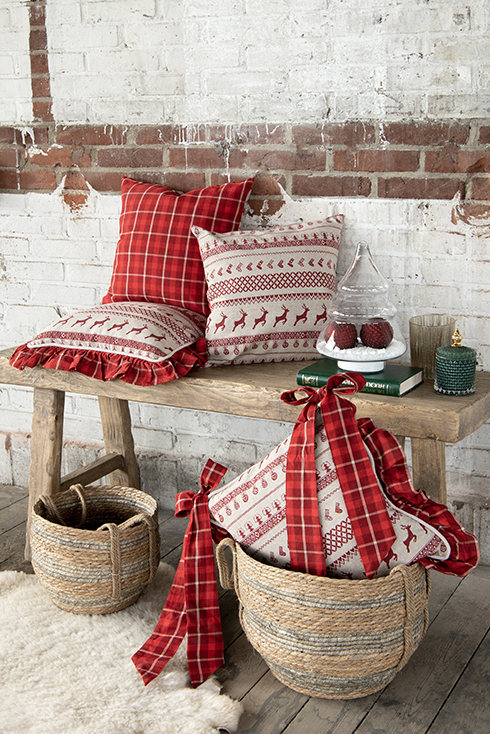 Un interno natalizio con due cuscini rossi classici e due cuscini per sedia rossi classici, e sulla panca di legno c'è anche una campana di vetro con vasi e due cesti rotondi per terra