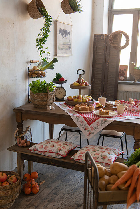 A farmhouse dining table with an apple-themed tablecloth, apple chair cushions, and rural dinnerware