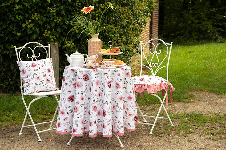 A bistro set outside with a romantic tablecloth and romantic chair cushions, and a high tea set on the table
